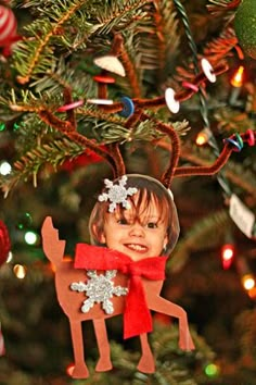 a christmas ornament hanging from a tree with lights in the background and a photo of a child on it