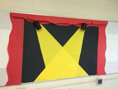 a large piece of art hanging on the wall in a school room with red, yellow and black colors