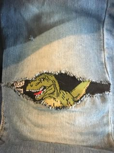 the back pocket of a pair of jeans with an embroidered t - rex on it