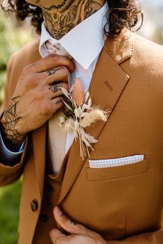 a man in a brown suit with tattoos on his face and hands, adjusting his tie