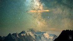 the night sky is filled with stars above mountains and snowcapped peaks, as well as an airplane flying over them