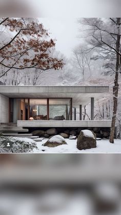 a house in the woods with snow on the ground and trees around it, surrounded by rocks