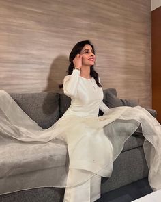 a woman sitting on top of a couch wearing a white dress and holding her hand up to her ear