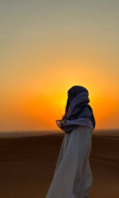 a woman standing in the desert at sunset with her head bowed back and veil draped over her face