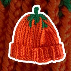 an orange knitted hat with green leaves on it and a sticker that says pumpkin