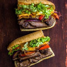 two sandwiches with meat, lettuce and tomato on them sitting on a wooden table