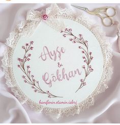 an embroidered name on a white doily next to some scissors and lace with pink flowers