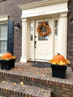 two black planters with pumpkins are on the front steps of a brick house