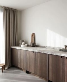 a kitchen with wooden cabinets and marble counter tops in front of a window that has drapes on the windowsill