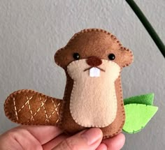 a hand holding a stuffed animal that is brown and white with a green leaf on it