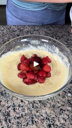 a bowl filled with batter and strawberries sitting on top of a counter next to a woman