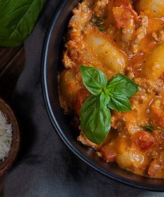 a bowl filled with meat and potatoes covered in sauce, garnished with basil leaves