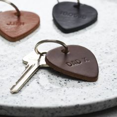 three heart shaped leather keychains with the word dad engraved on them sitting on a marble surface