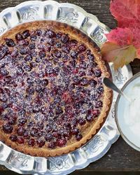 a pie sitting on top of a metal tray next to a bowl of cream and an autumn leaf