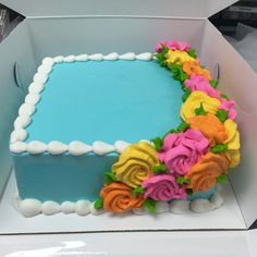 a blue and yellow cake with flowers on it sitting in a white box, ready to be eaten