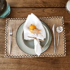 a place setting on a wooden table with silverware and an orange in the center