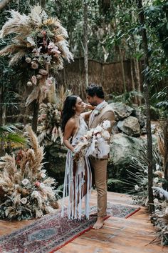 a newly married couple standing in front of an arch with flowers and feathers on it