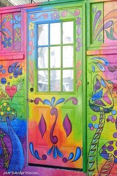 a colorful painted building with a green door and window on the outside wall is decorated with flowers and leaves