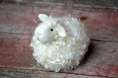 a white sheep with curly hair sitting on top of a wooden floor next to a pink and purple background