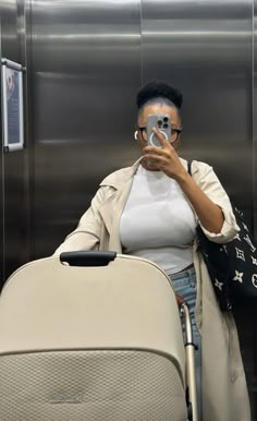 a woman taking a selfie with her cell phone in front of an airport elevator