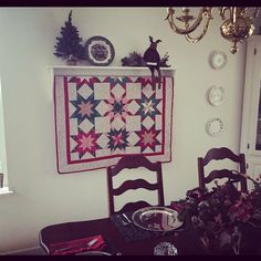 a dining room table with a quilt hanging on the wall