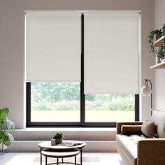 a living room with a couch, coffee table and large window covered in white roller shades