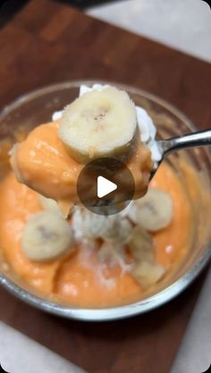 a bowl filled with bananas and cream on top of a wooden cutting board next to a spoon