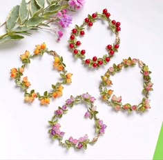 four different bracelets with flowers and leaves on the top one is red, pink, yellow and green