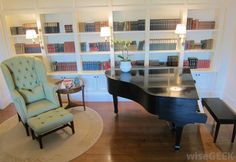 a living room with a piano, chair and table in front of bookshelves