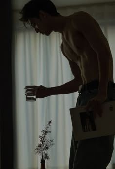 a shirtless man holding an empty glass in his hand and looking down at the floor