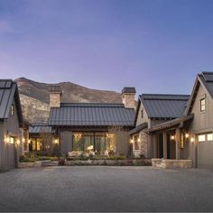 a large house with lots of windows and lights on it's front porch, surrounded by mountains