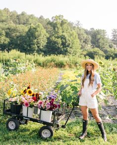 a woman standing next to a wheelbarrow with sunflowers in the background