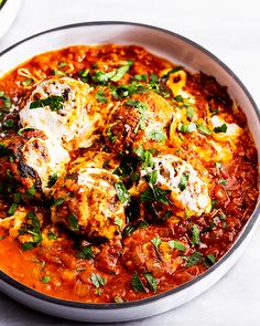 a bowl filled with meat and cheese covered in tomato sauce, garnished with parsley