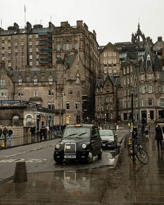 a black car driving down a wet street next to tall buildings and people walking on the sidewalk