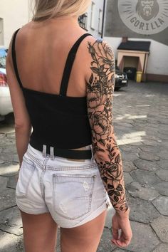 the back of a woman's body with tattoos on it and flowers in her left arm