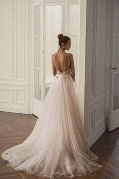 a woman in a wedding dress is standing by a wall with her back to the camera