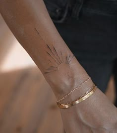 a woman's arm with a gold bracelet and sun tattoo on her left wrist