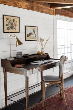 a desk and chair in a room with wood beams on the ceiling, along with two framed pictures