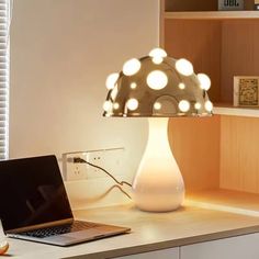 a laptop computer sitting on top of a wooden desk next to a white vase filled with lights