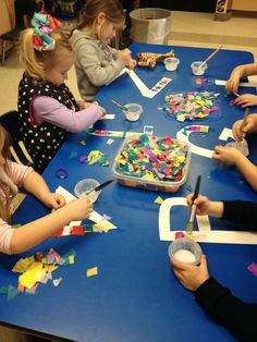 several children are sitting at a table making crafts with scissors and construction paper on them