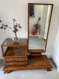 a wooden table topped with a mirror next to a vase filled with flowers and a violin