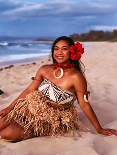 a woman sitting on the beach wearing a hula skirt and flower in her hair