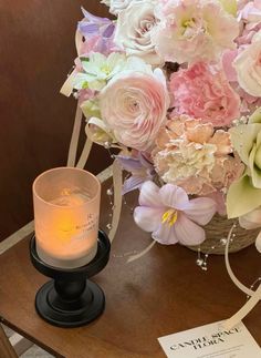 a vase filled with pink and white flowers next to a lit candle on a table