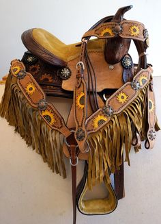 a saddle with sunflowers on the side and fringed leather, sitting on a white surface