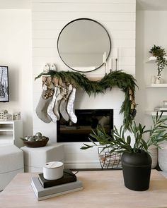 a living room decorated for christmas with stockings hanging from the mantel and potted plants