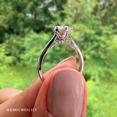 a woman's hand holding an engagement ring in front of a window with trees