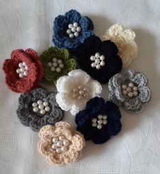 six crocheted flowers are arranged on a white tablecloth, with pearls in the center