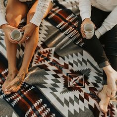 two women sitting on a blanket holding coffee cups