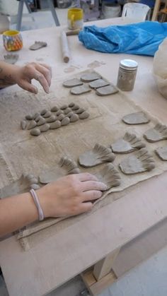 a woman is making clay shapes on a table with other items around her and one hand reaching for them