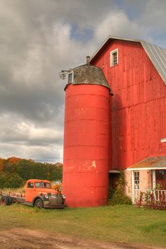 an old red truck parked in front of a barn with a silo on it